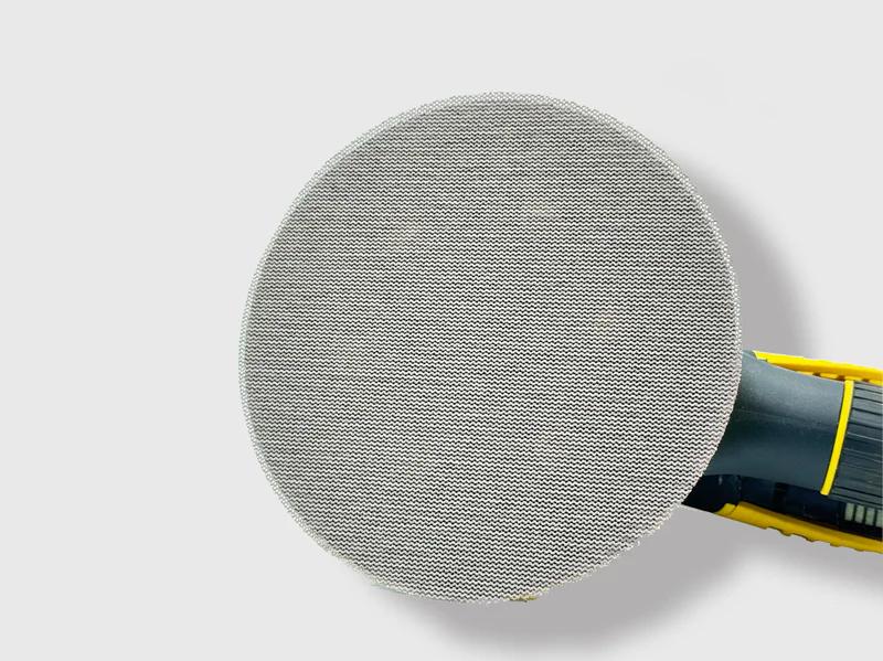 Gray mesh net sanding disc with aluminum oxide grain attached to power sander in workshop setting