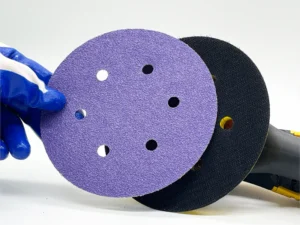 Purple zirconia alumina sanding disc product image, multi-hole, held by gloved hand, white background